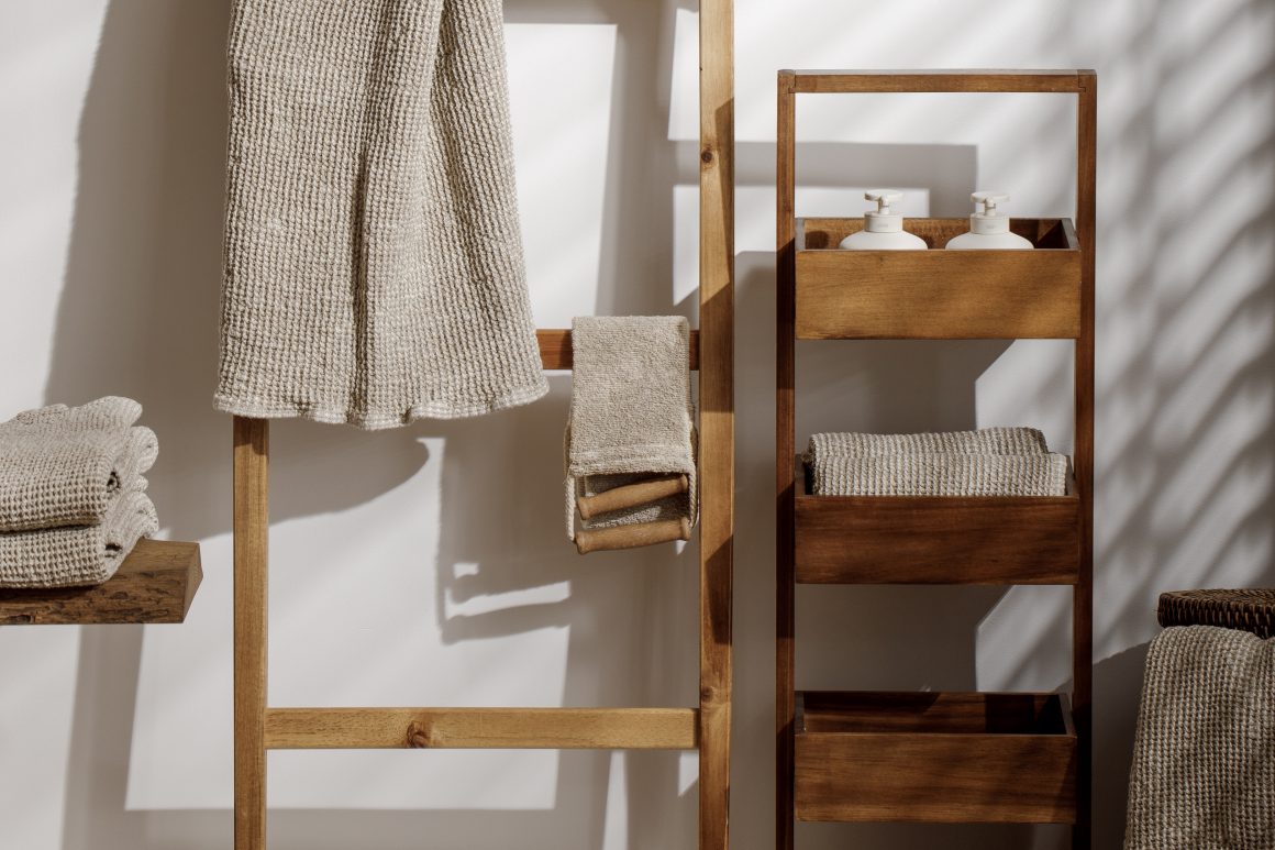 Serviettes et linge de bain beige en coton texturé rangés sur porte-serviettes et étagère en bois.
