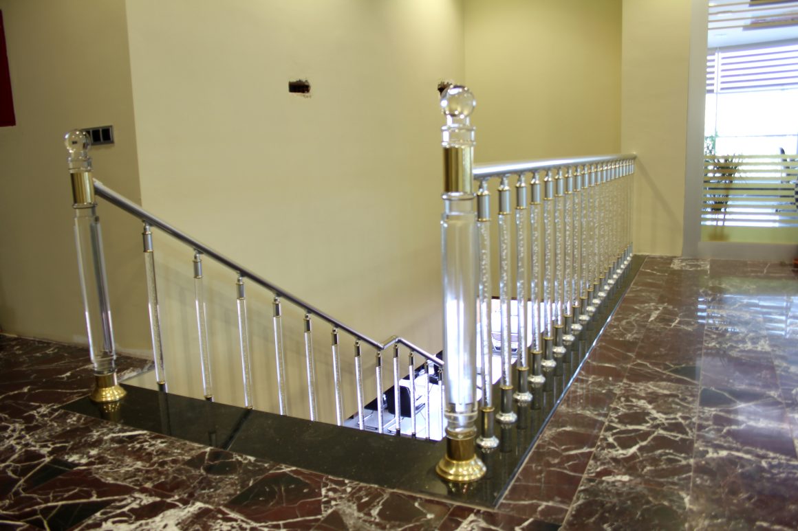 Rampe d'escalier élégante en métal poli et verre, sol en marbre brun et murs crème.