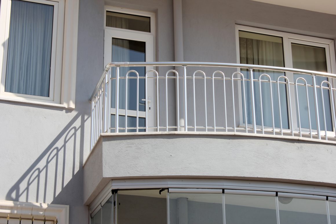 Balcon moderne, avec garde corps en inox, fixé à façade grise d’un immeuble.