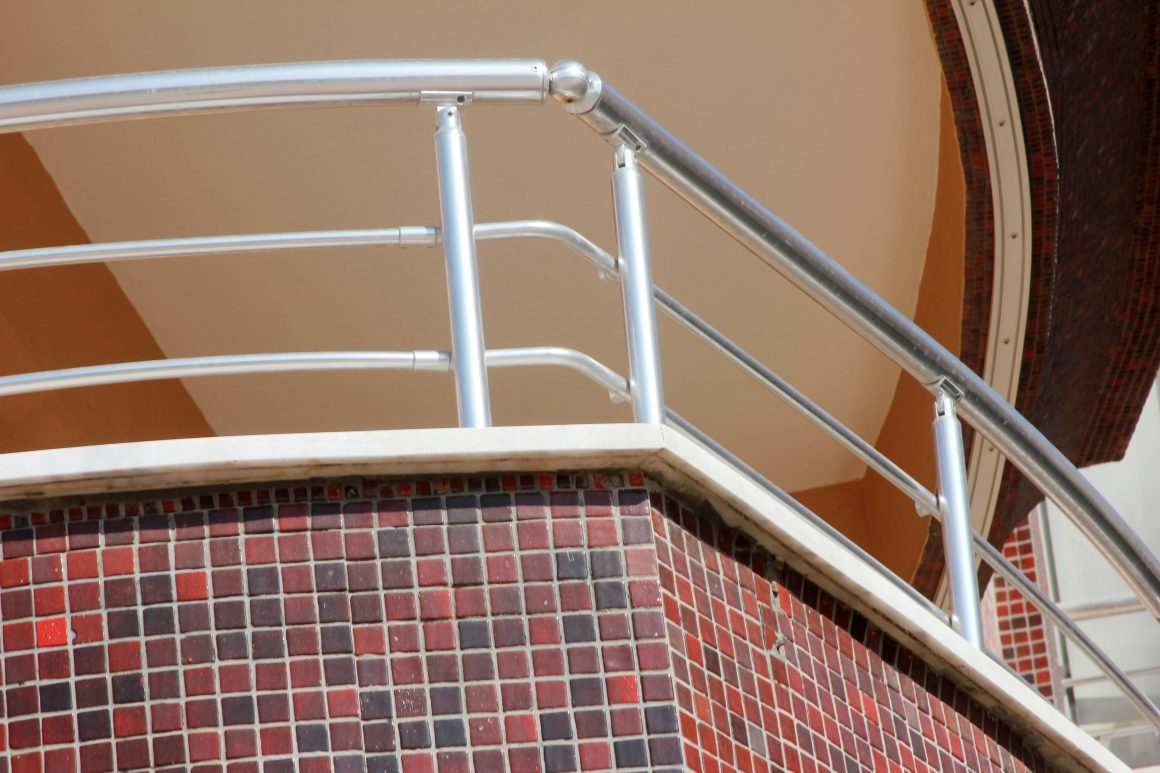 Terrasse extérieur avec un garde-corps en inox et un mur carrelé rouge et marron.