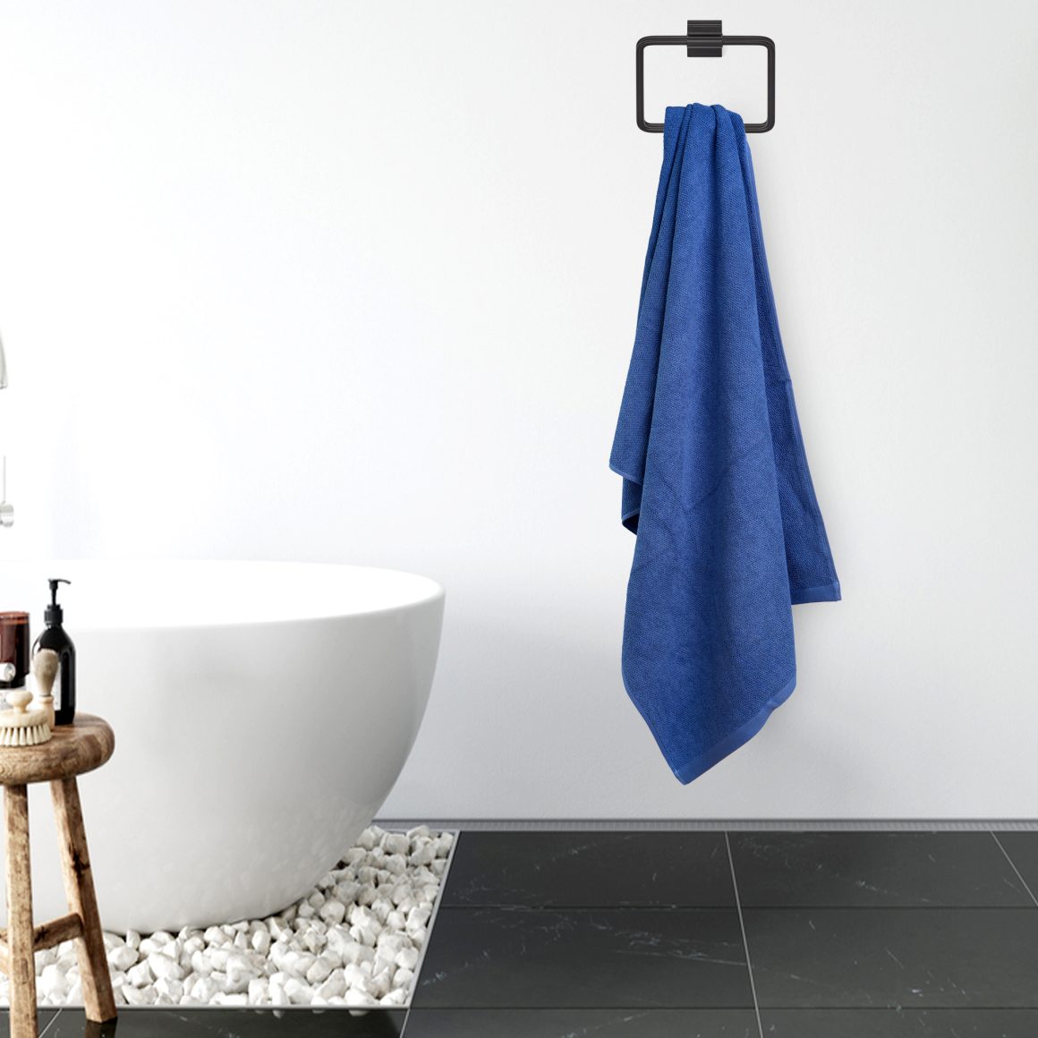 Serviette suspendue sur crochet noir dans une salle de bains moderne blanche avec carrelage noir et baignoire.