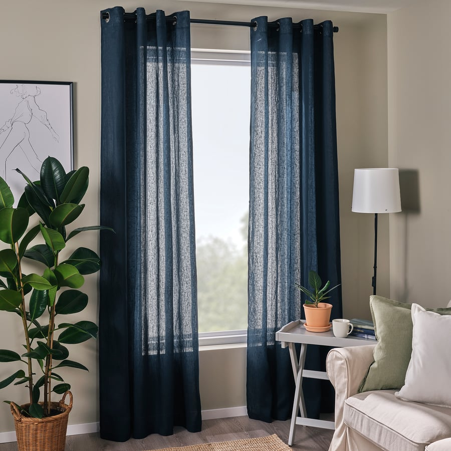 Intérieur zen avec rideaux bleu marine semi-transparents, plante, canapé beige et lampe sur table grise.