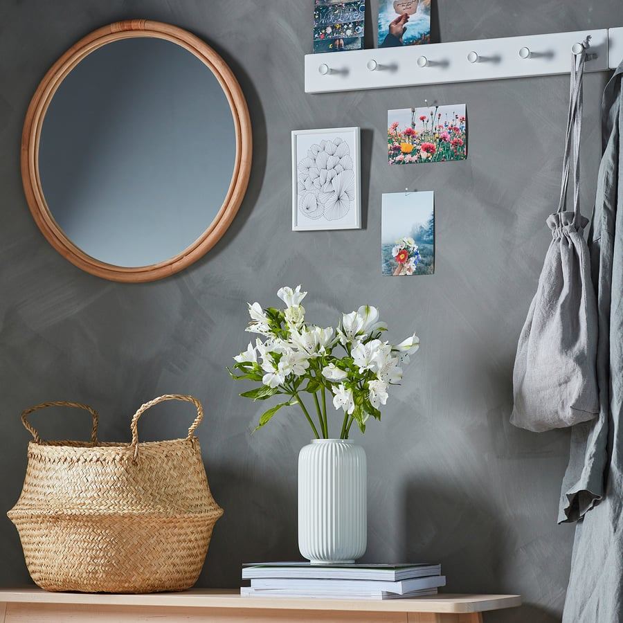 Intérieur zen et chaleureux incluant miroir, vase avec fleurs, panier tressé, photos colorées et porte-manteau blanc.