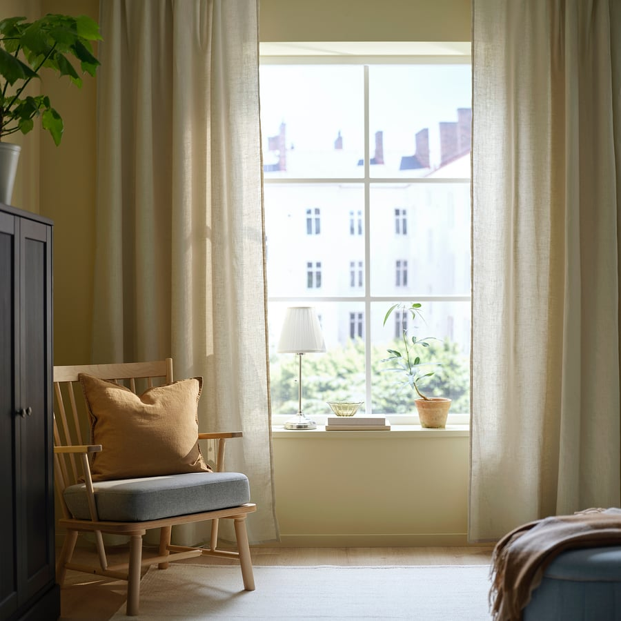 Coin lecture zen et lumineux avec fauteuil en bois, rideaux beige, lampe sur rebord et plante.