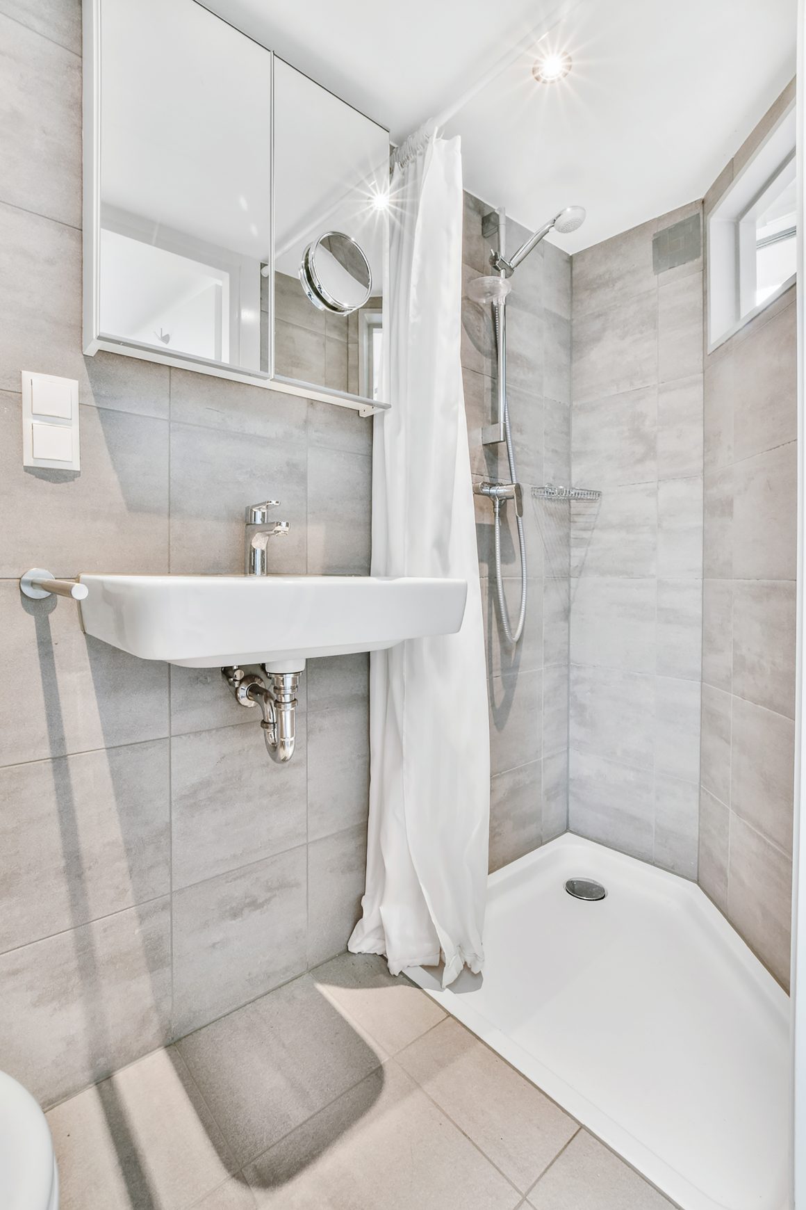 Salle de bain lumineuse avec miroir, spots, carrelage gris grand format, lavabo et douche