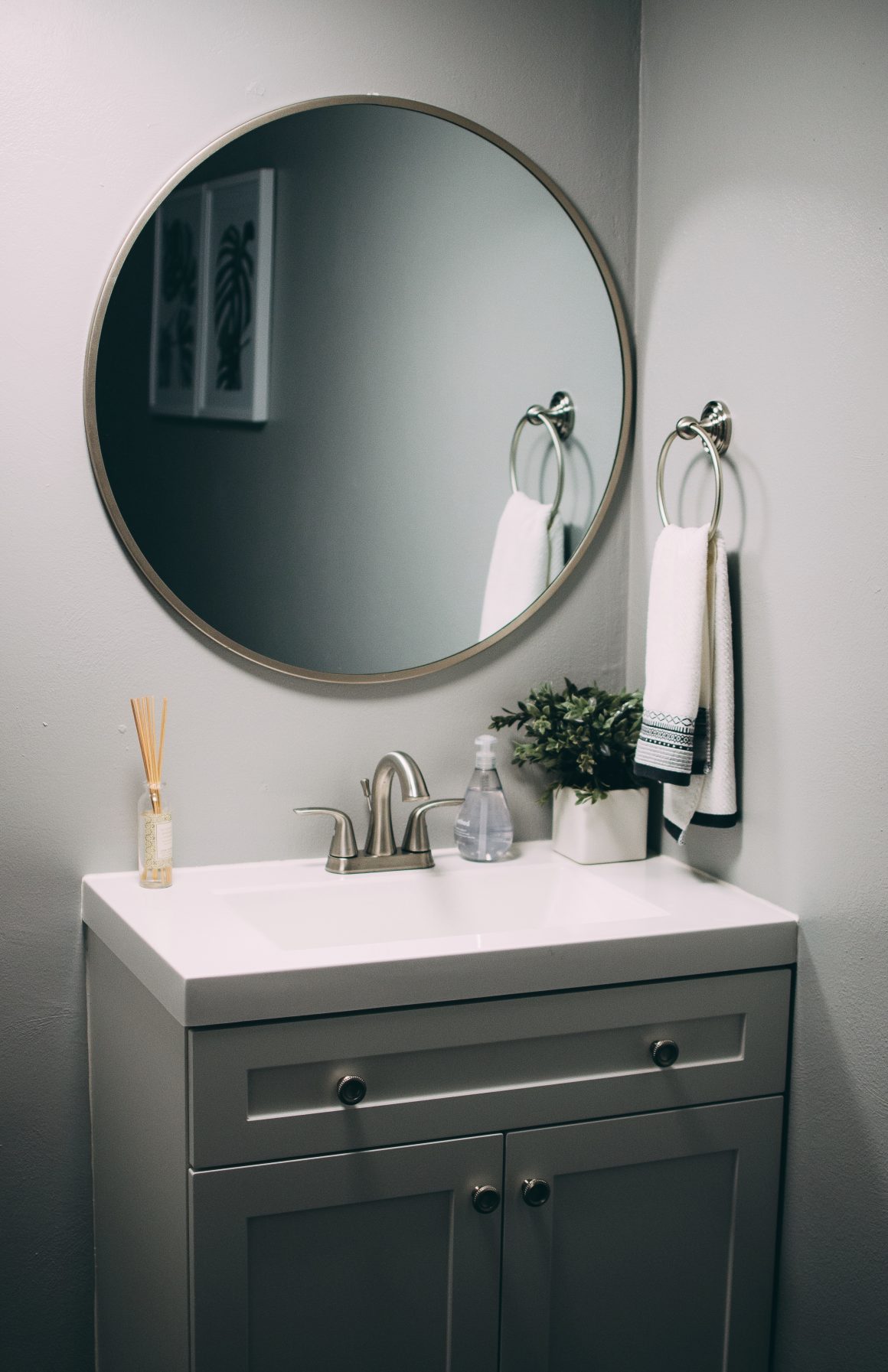 Petit lavabo moderne avec miroir rond, serviette blanche et plante verte.