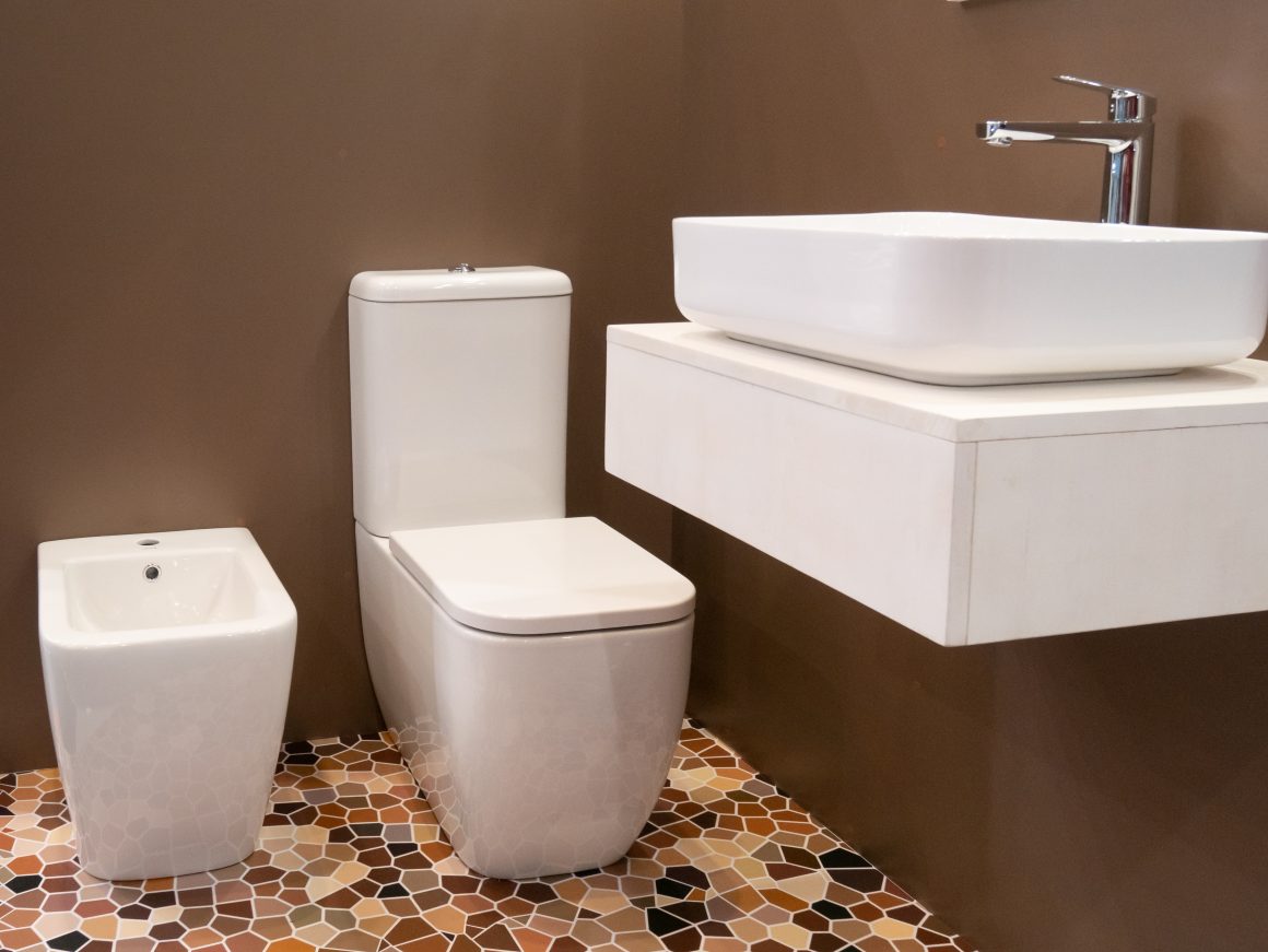 Salle de bain moderne avec mur marron, sol carrelage motifs géométriques, lavabo blanc suspendu et toilettes.
