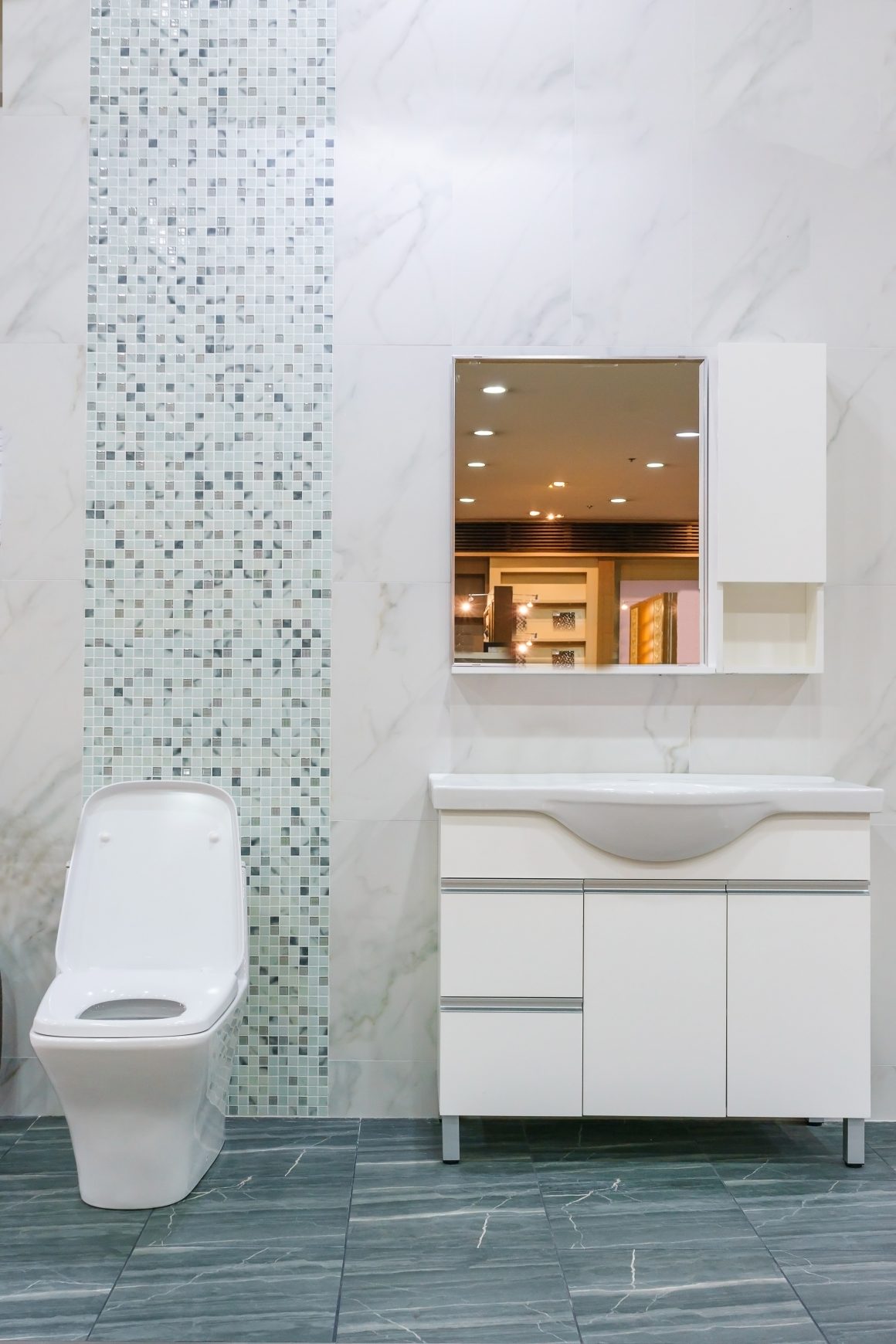 Toilettes blanches avec meuble lavabo, miroir et carrelage gris et blanc.