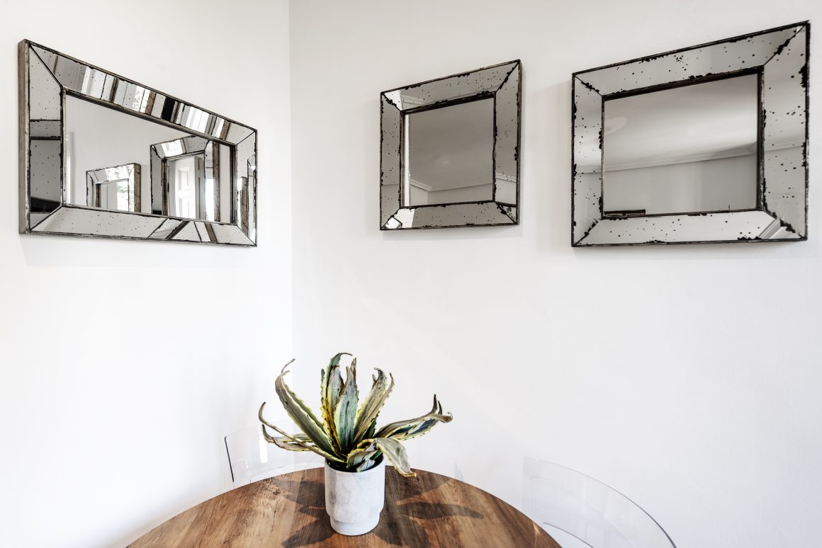 Trois miroirs vintage vieillis placés sur deux murs blancs, créant de la profondeur et du caractère dans l’espace.