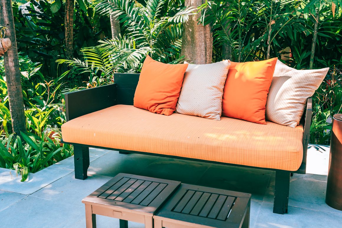 Canapé orange avec coussins, entouré de verdure luxuriante sur une terrasse ensoleillée.