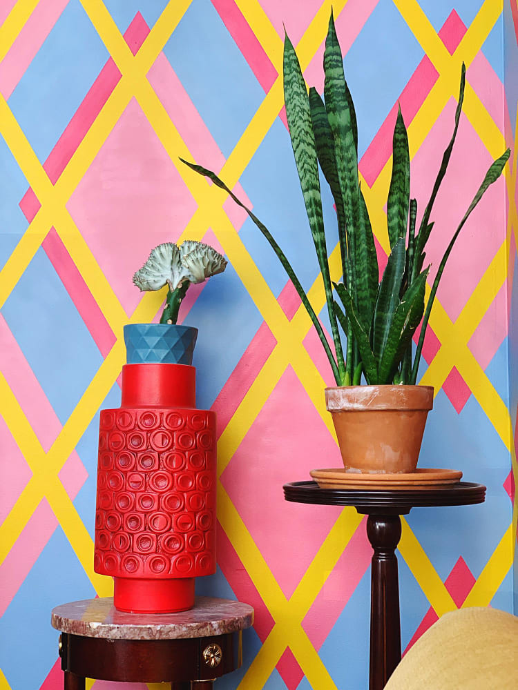 un mur très coloré avec des rayures pastel jaune, bleu et fuchsia, et deux pots de fleurs aux couleurs vives