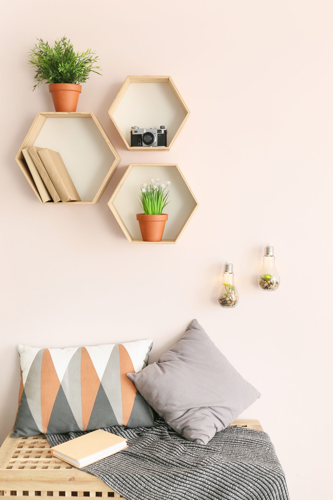 Mur rose avec des étagères hexagonales en bois, incluant des plantes en pots et livres