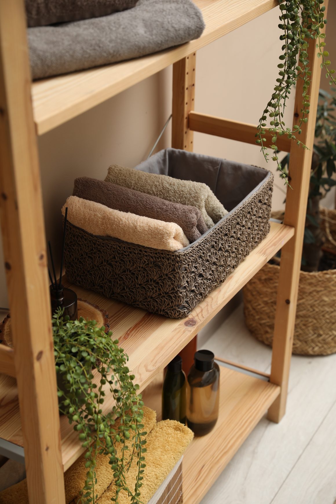 Étagère en bois avec serviettes pliées, paniers, bouteilles et plantes vertes