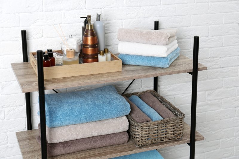 Plateau en bois contenant produits cosmétiques avec des étagères et un panier tressé servant à ranger serviettes salle de bain.