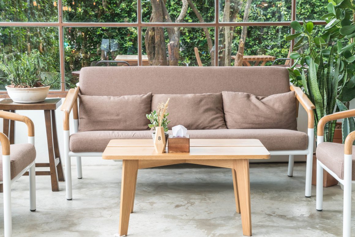 Salon de jardin design avec canapé beige, coussins, table en bois et plantes vertes.