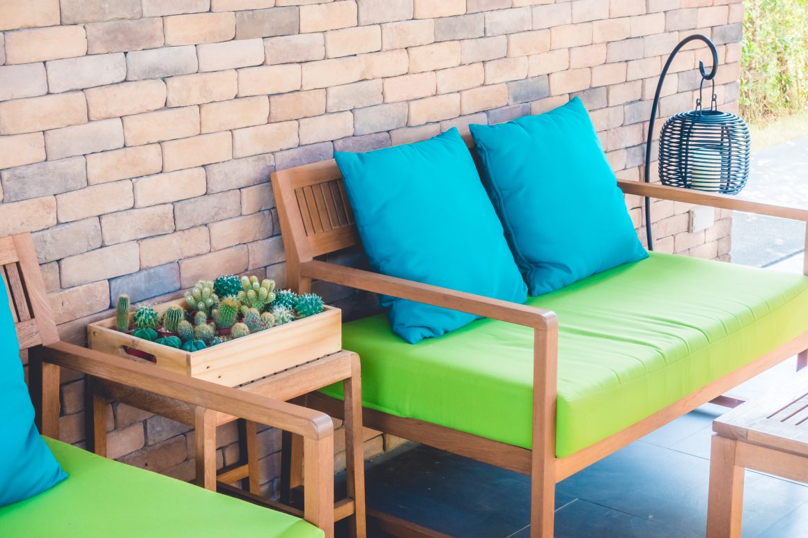 Salon de jardin avec canapé en bois, coussins bleus, assise verte et lanternes décoratives.