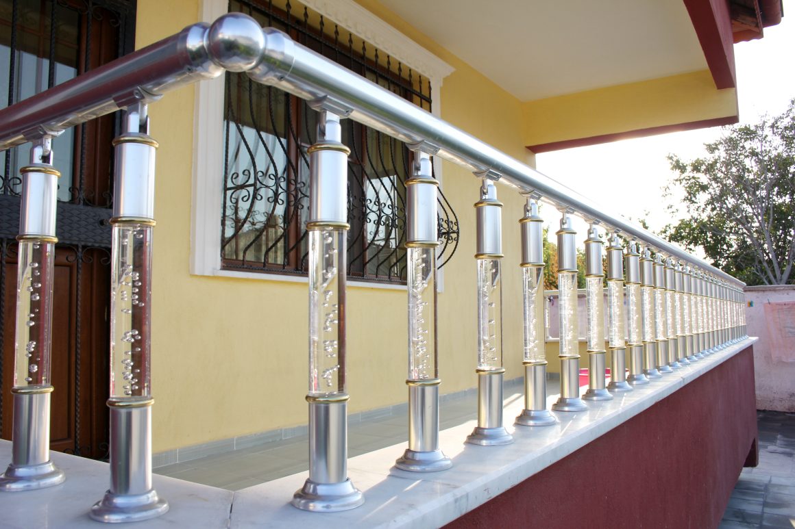 Balustrade en métal et verre avec bulles décoratives, devant maison jaune avec fenêtre et porte.