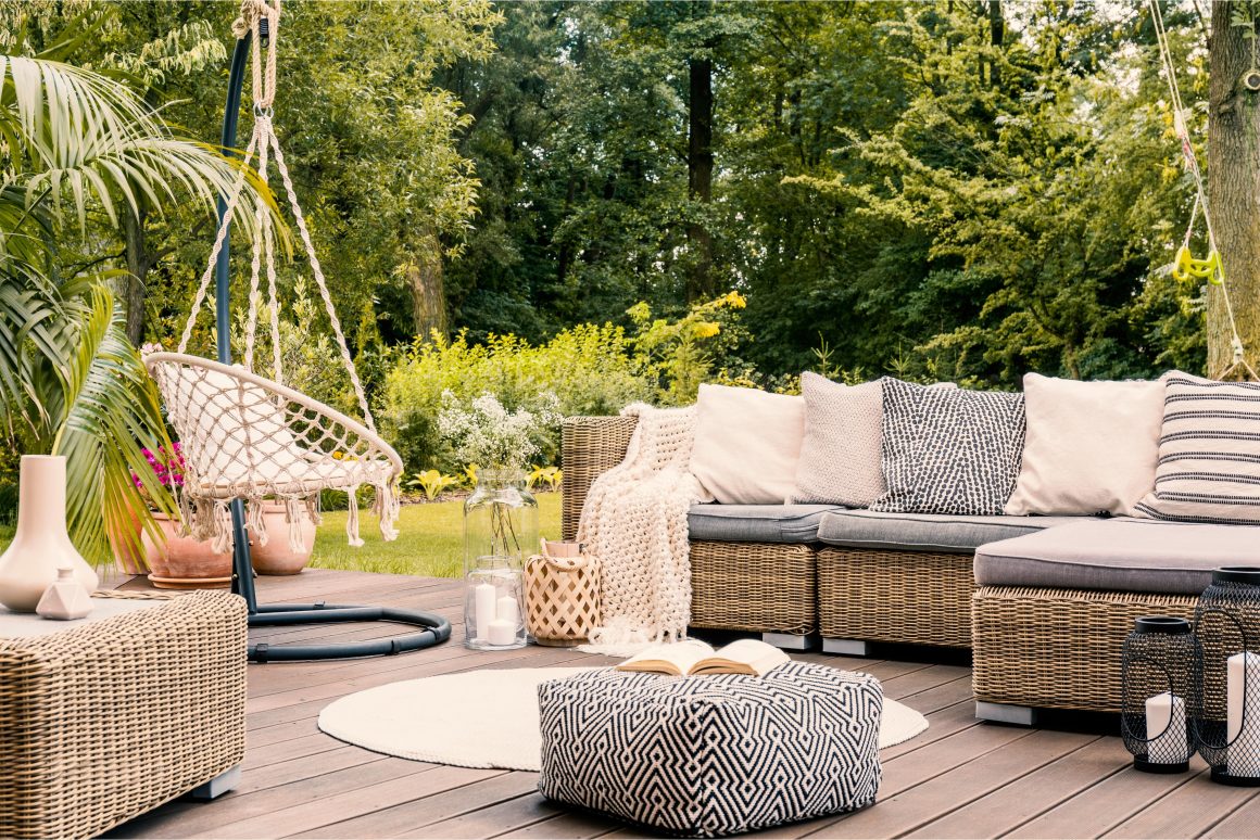 Espace extérieur chaleureux avec mobilier en osier, coussins variés et fauteuil suspendu.