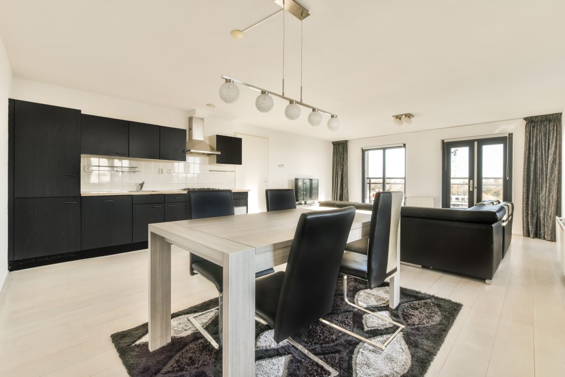 espace ouvert lumineux et minimaliste incluant table en bois, chaises noires, canapé cuir et cuisine noire intégrée