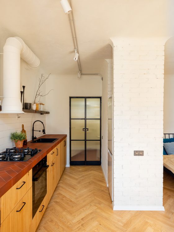 Aménager studio 18m2 avec cuisine ouverte, placards en bois, étagère murale, colonne briques blanches et lit
