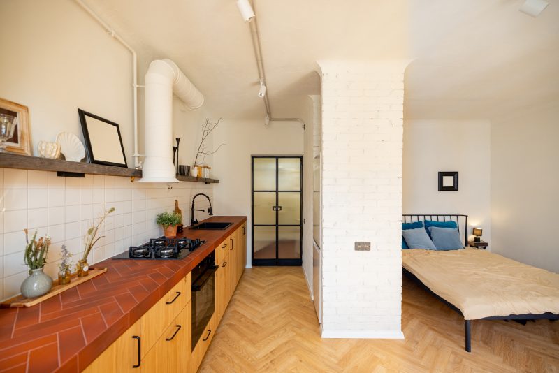 Aménager studio 18m2 avec cuisine ouverte, placards en bois, étagère murale, colonne briques blanches et lit