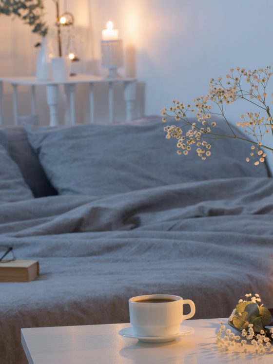 Chambre incluant lit gris, bougie allumée, vase avec fleurs : atmosphère apaisante et relaxante