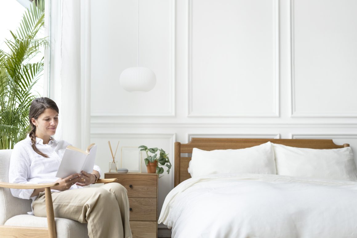Femme détendue lisant dans une chambre apaisante avec déco minimaliste, meubles en bois et plante
