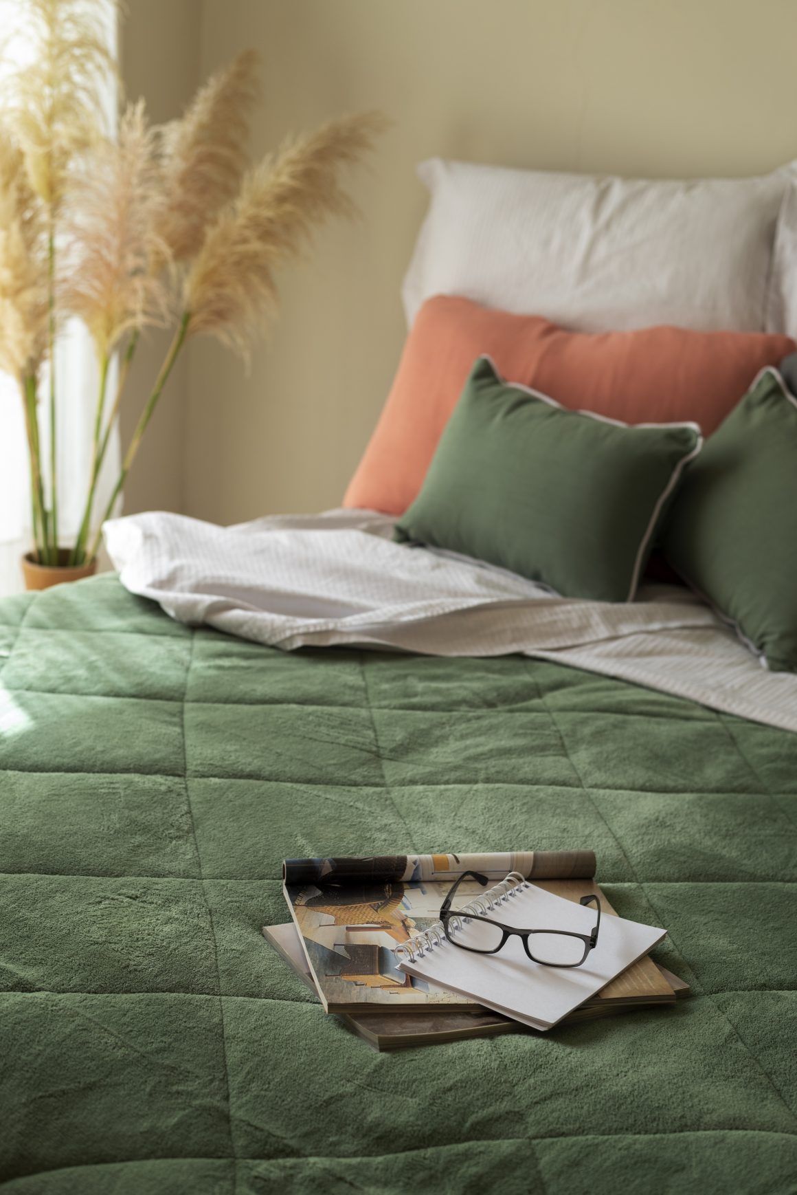 Chambre apaisante incluant un lit douillet avec couette verte, coussins verts et corail, et plantes décoratives