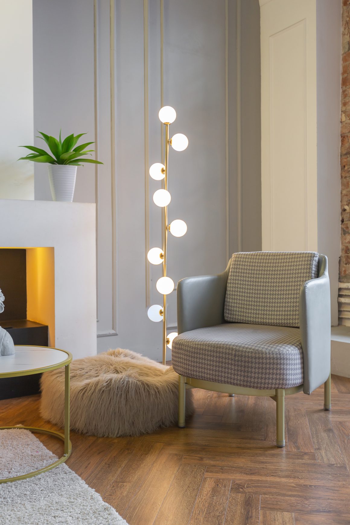 Salon élégant et cosy incluant fauteuil gris, lampadaire globe doré, pouf fourrure et plante verte