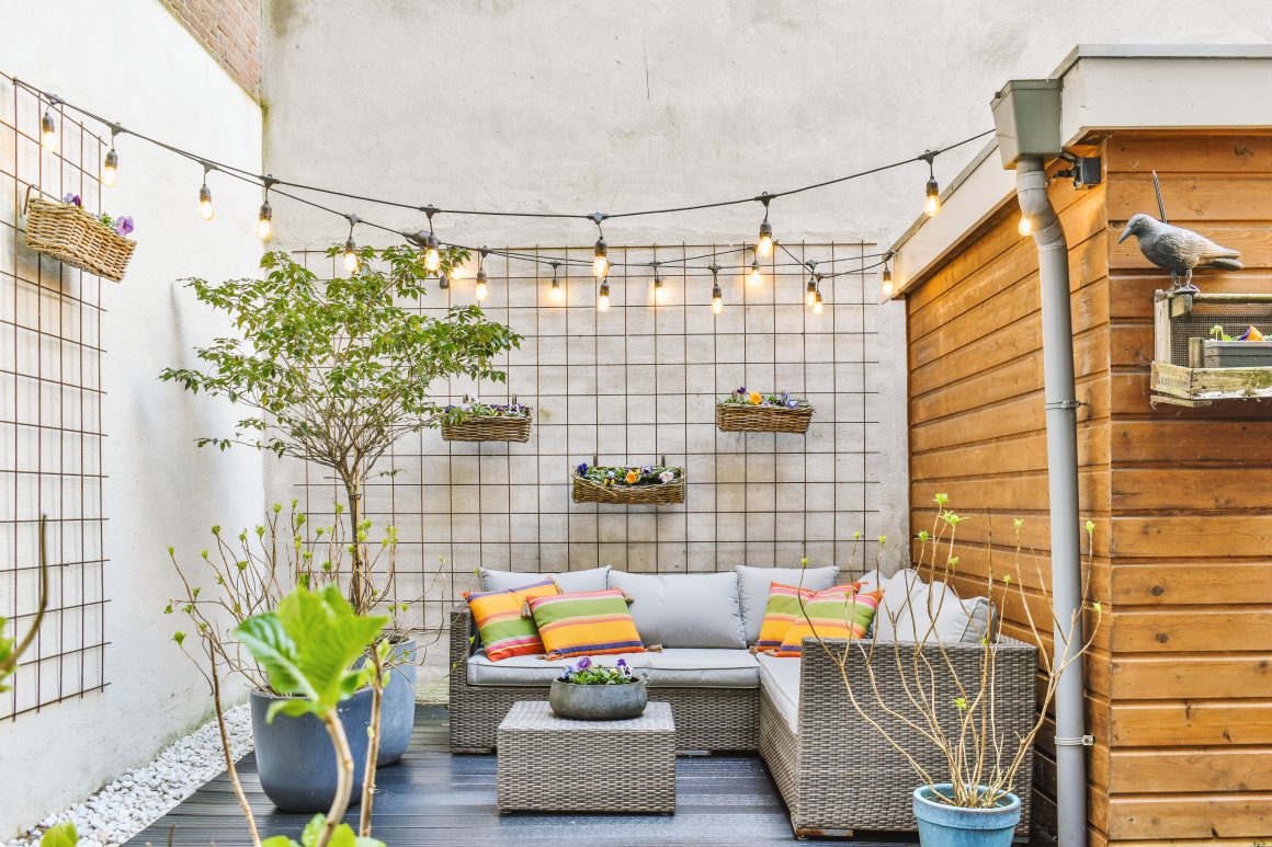 Un coin terrasse cosy incluant canapé en rotin, coussins colorés, guirlandes lumineuses, plantes en pots