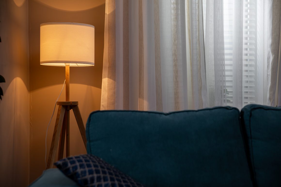 Lampe sur trépied éclairant doucement un salon chaleureux avec rideaux translucides et canapé bleu