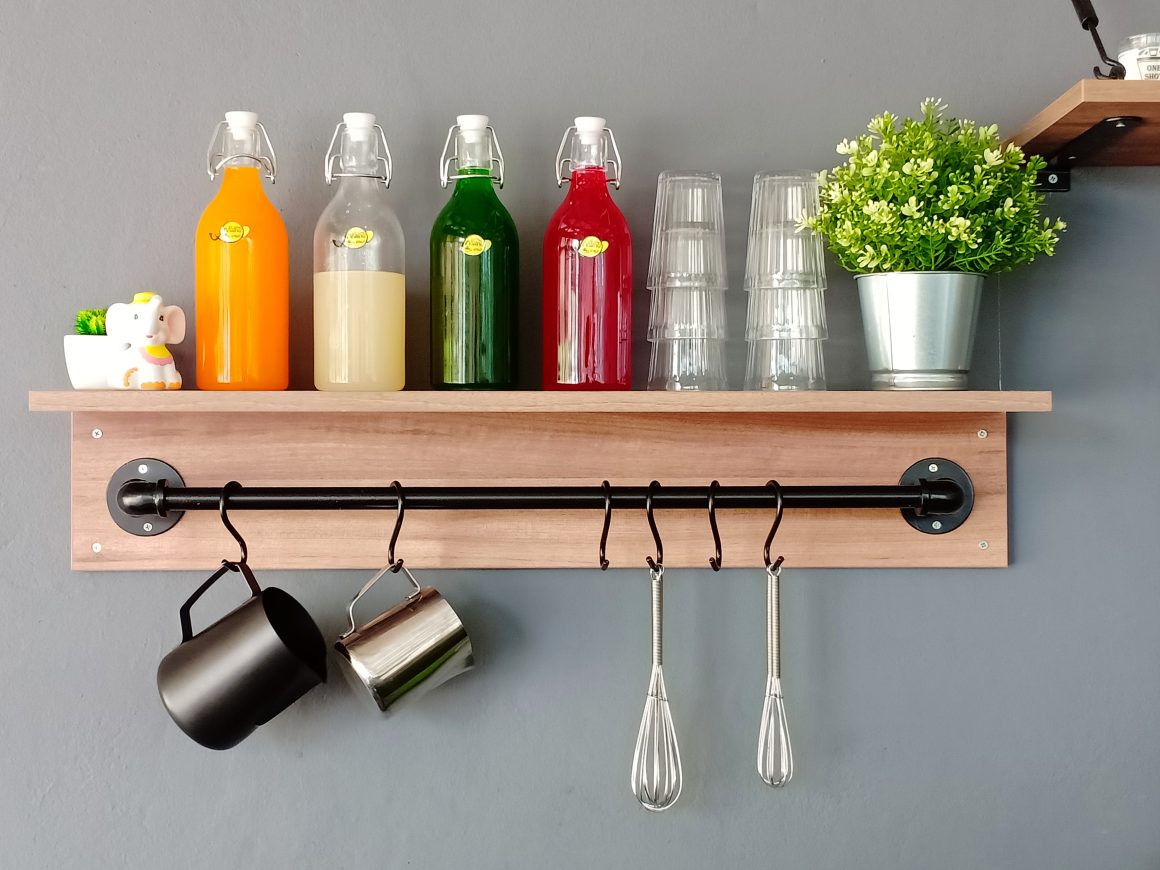 Étagère murale moderne avec bouteilles colorées, verres, plante et crochets tenant tasses et fouets.