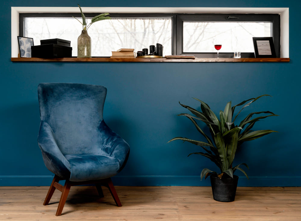 un fauteuil bleu canard à côté d'une plante verte, sur un sol en parquet