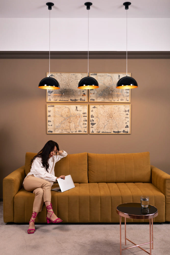 une femme assise dans un canapé ocre sous trois lampes domes suspendues