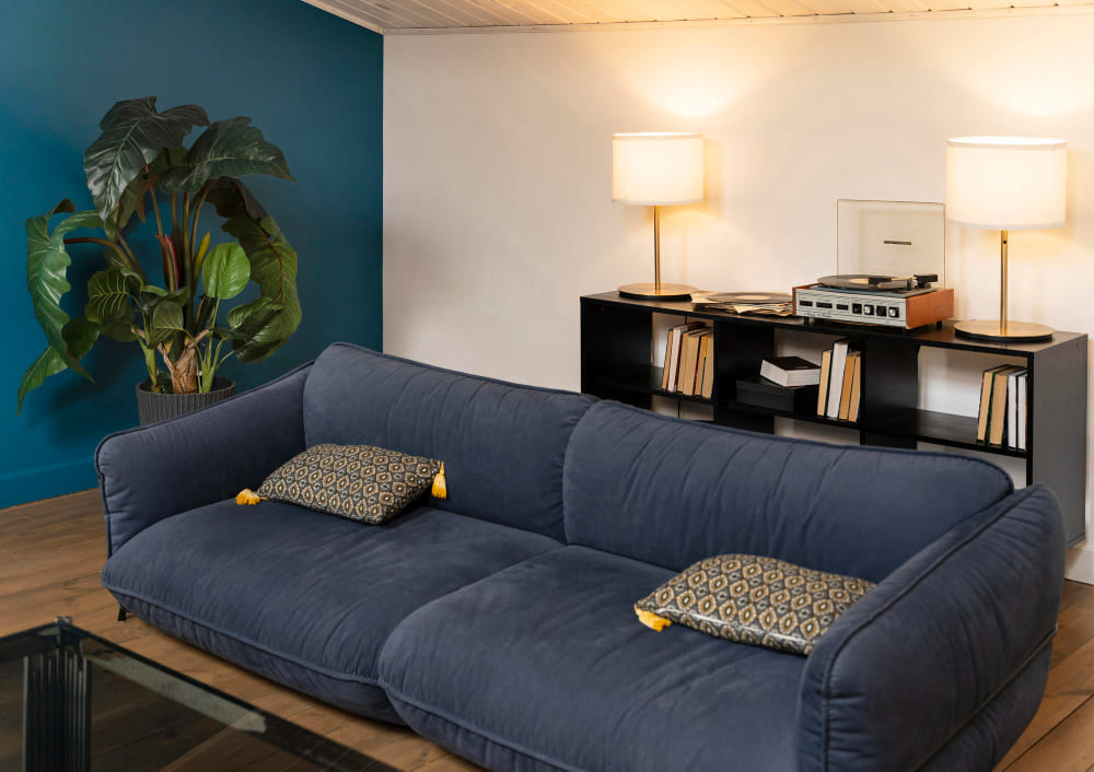 un grand canapé cocooning bleu marine avec des coussins à motifs et du parquet au sol