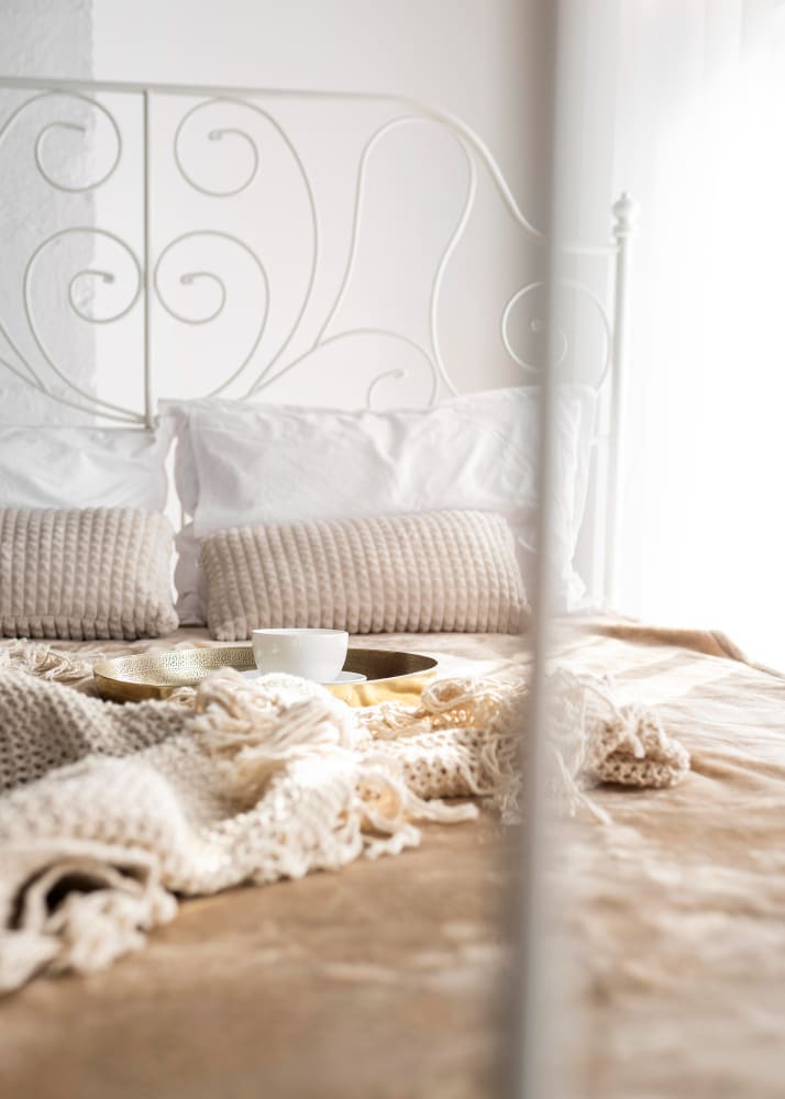 un grand lit tendance en fer forgé dans une chambre lumineuse avec une couverture nude