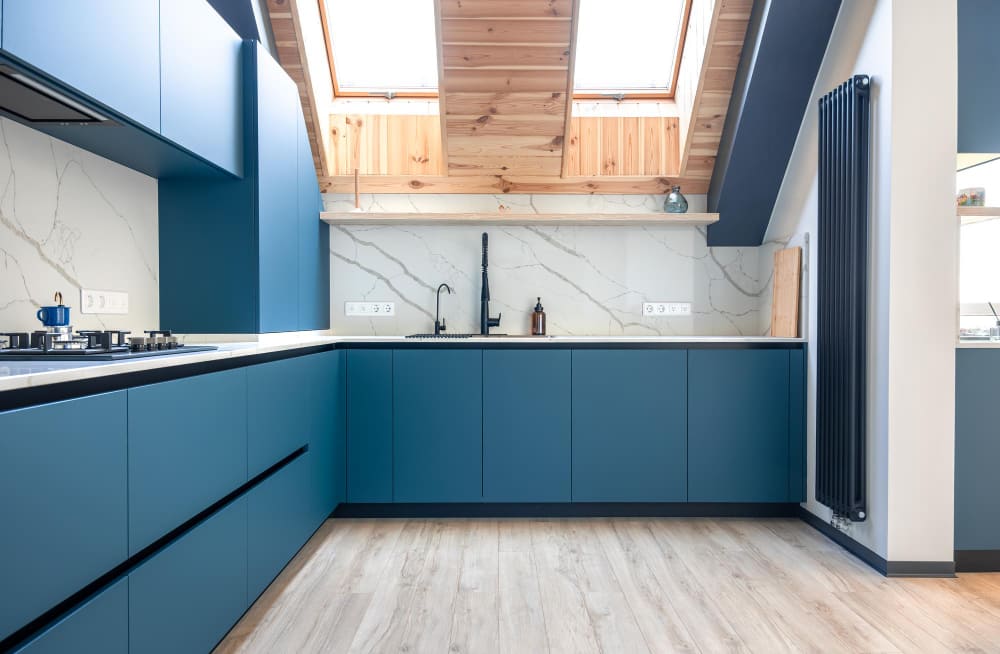 une grande cuisine couleur bleu pétrole, avec un sol en parquet et des lambris au plafond