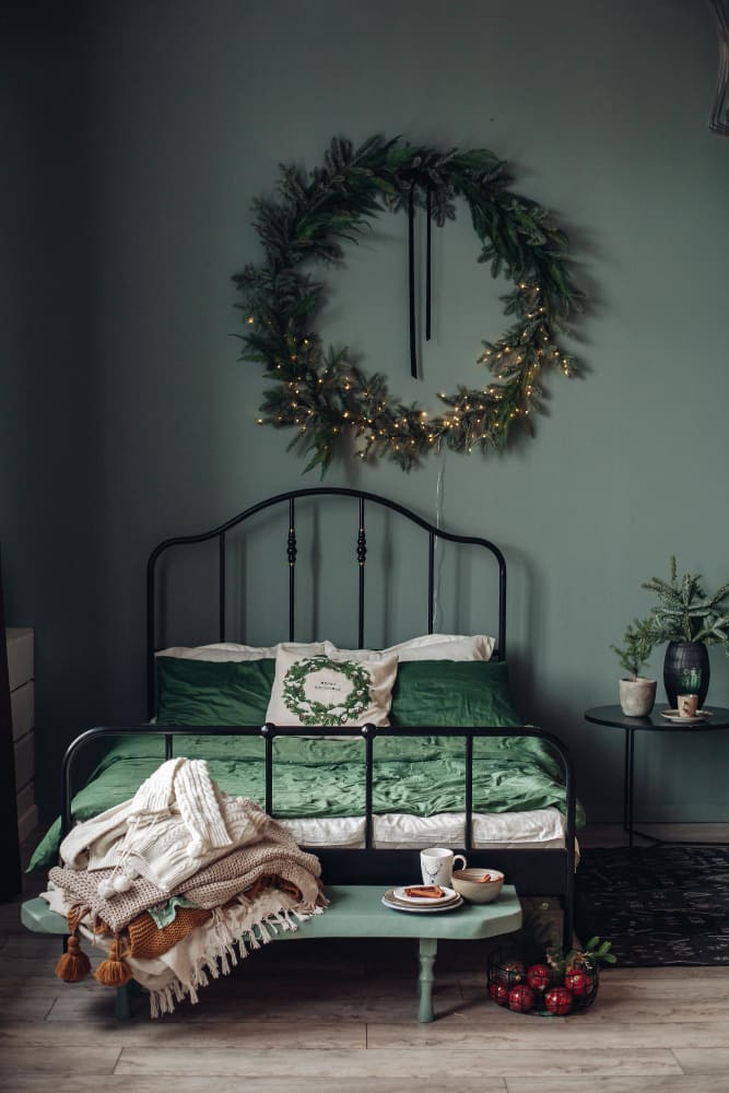 un lit en fer forgé avec le vert forêt couleur tendance 2026 tout autour, surmonté d'une couronne végétale