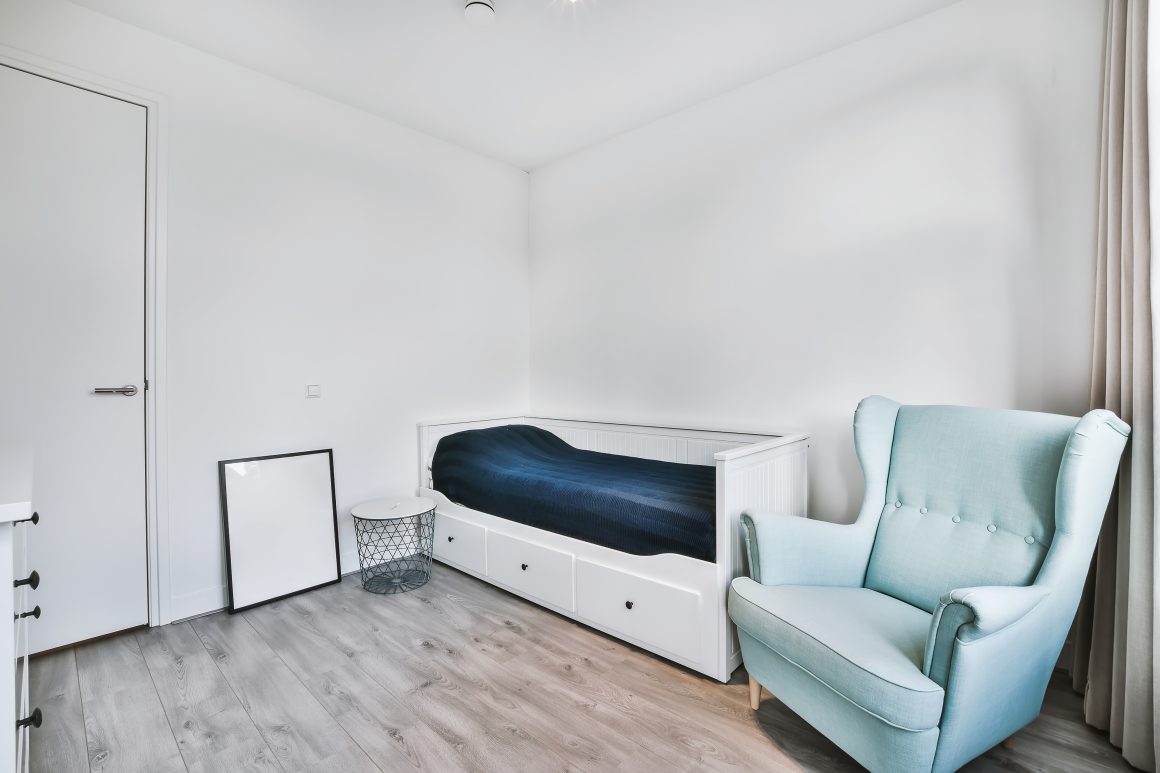 Intérieur minimaliste avec lit incluant des tiroirs, fauteuil, petite table basse et commode