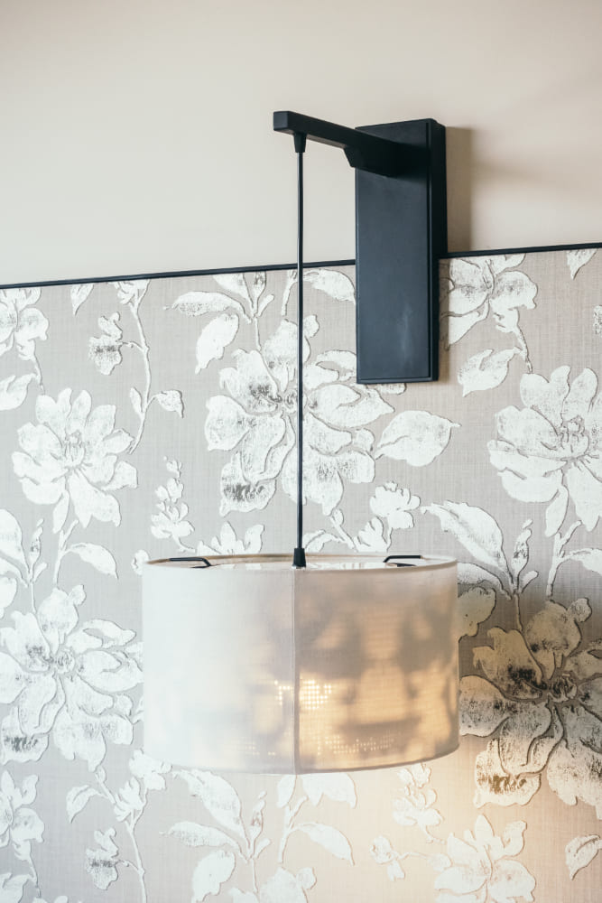 du papier peint fleuri derrière une applique tendance et un abat-jour suspendu