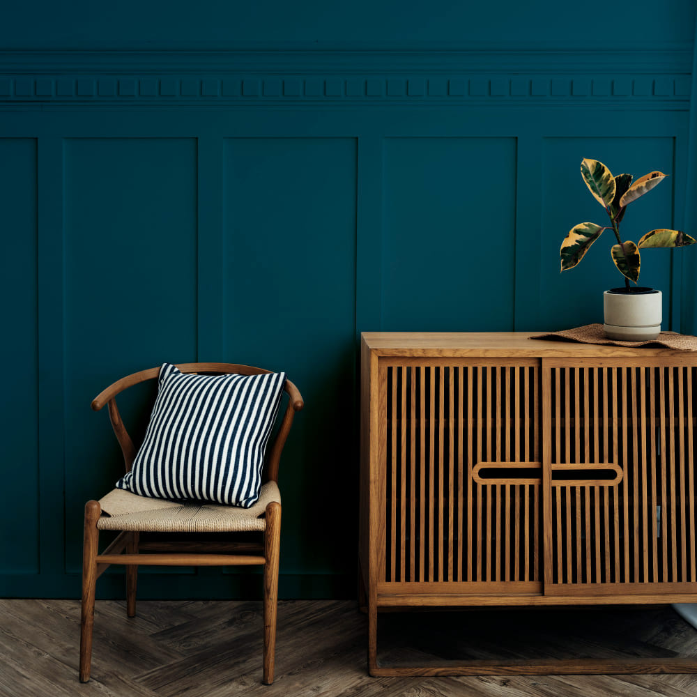 une pièce élégante avec du parquet chevrons, des soubassements bleu canard et un fauteuil et une commode en osier
