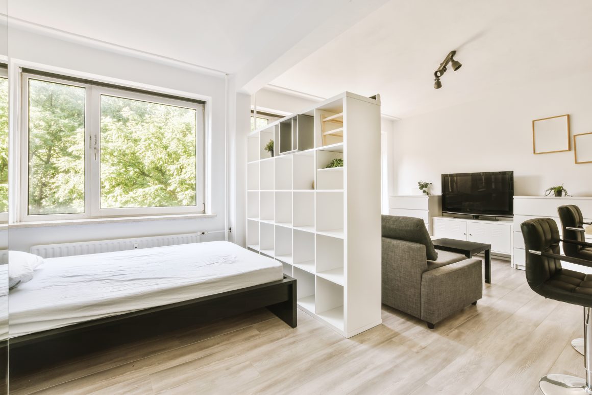 Coin nuit et salon séparés par des étagères avec table et meubles de rangement pour aménager studio 18m2
