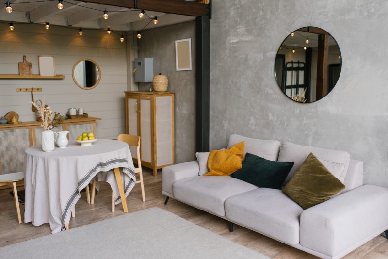Salon cosy avec canapé clair, coussins colorés, miroir rond, éclairage guirlande : la tendance déco 2026