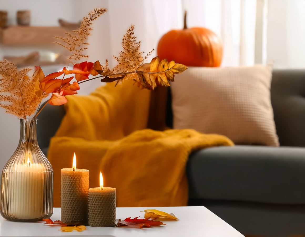 Décoration maison automne avec bougies, plaid moutarde, feuilles sèches et une citrouille décorative.