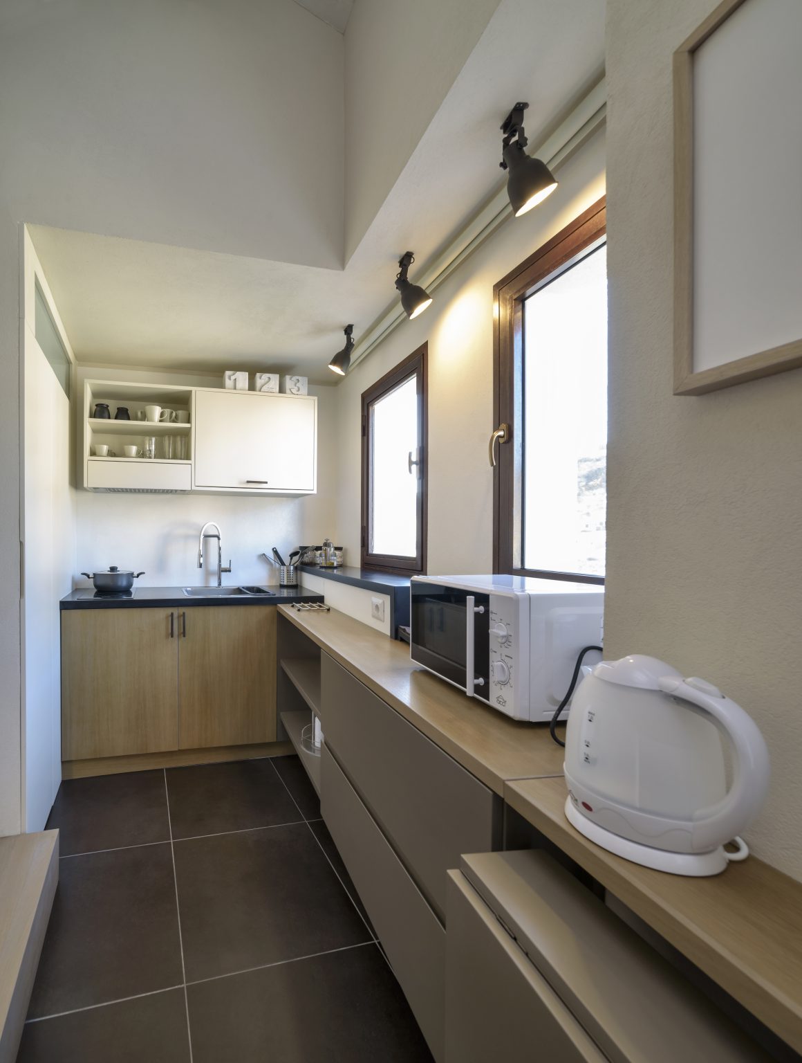 Petite cuisine incluant plans en bois, évier, micro-ondes, rangement ouvert et spots muraux.