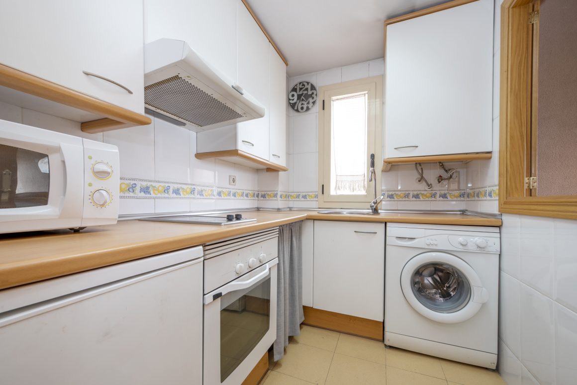 Cuisine compacte et fonctionnelle avec électroménagers blancs, plan de travail en bois et rangements.