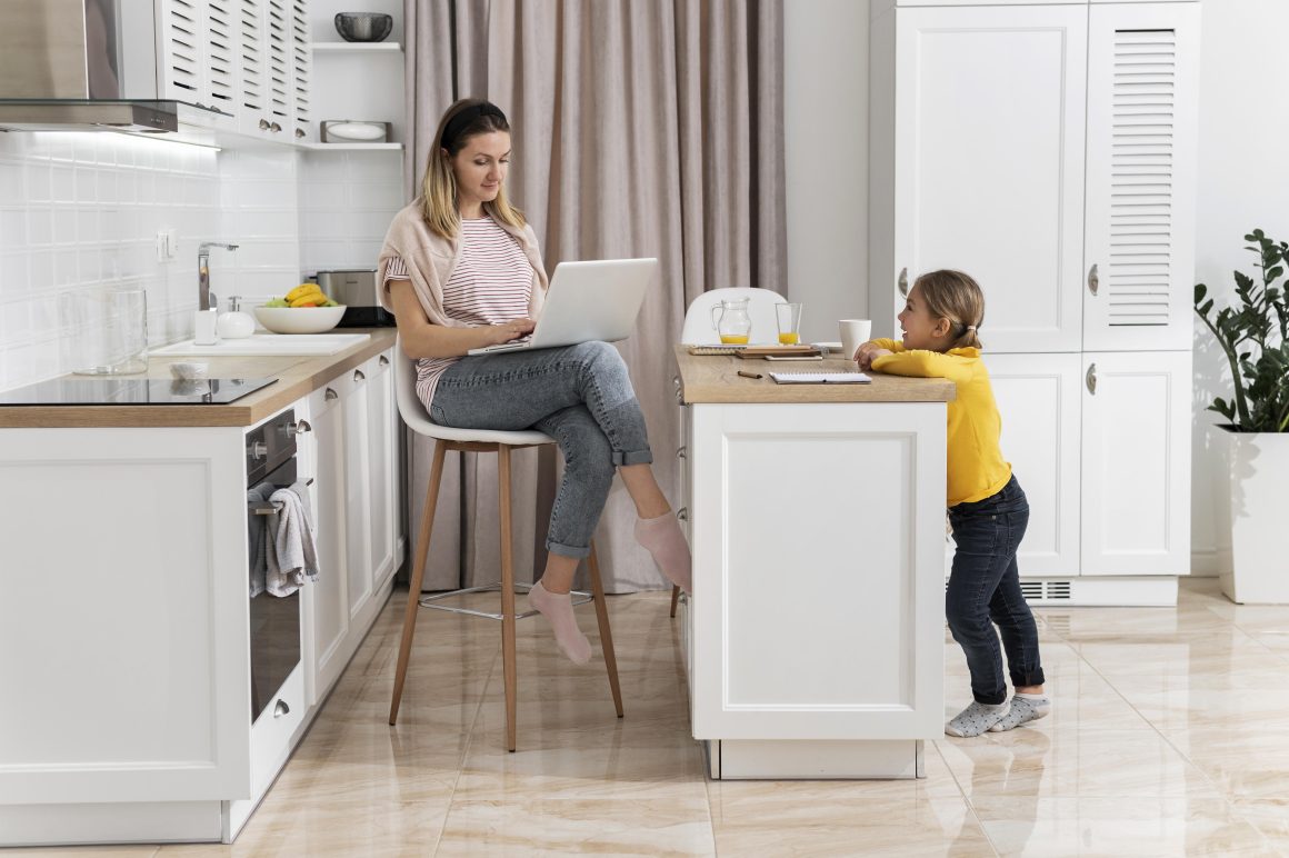 Femme avec sa fille dans une cuisine ouverte qui inclut îlot central, rideau, éléments de rangement et plante