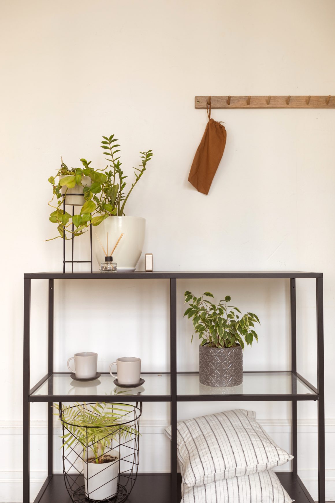 Étagères minimalistes en métal noir, plantes vertes, coussins rayés et tasses