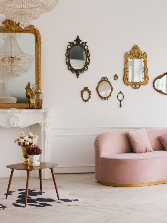 Déco salon vintage moderne incluant canapé rose pâle, fauteuil chic, miroirs dorés, cheminée et tapis.