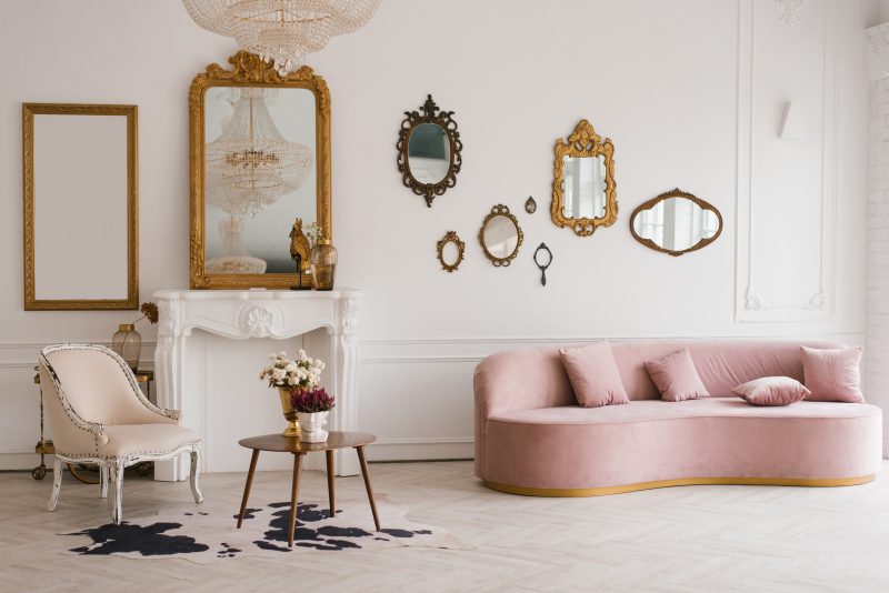 Déco salon vintage moderne incluant canapé rose pâle, fauteuil chic, miroirs dorés, cheminée et tapis.